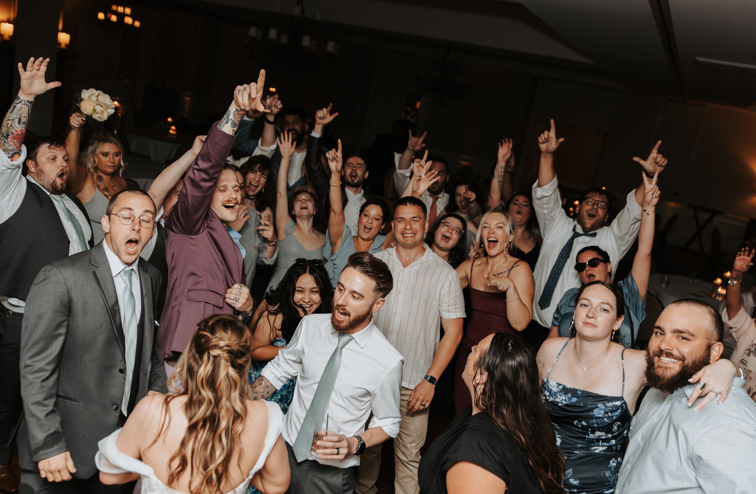 Wedding reception dance floor filled with celebrating guests under colorful lights.