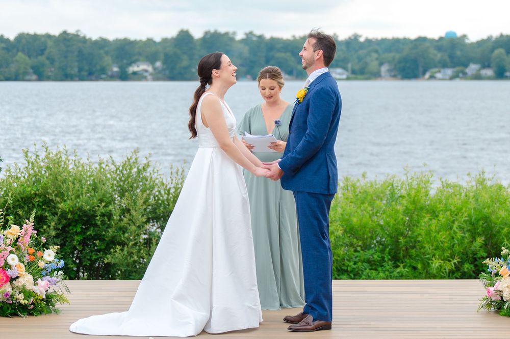 Wedding couple poses together on a lakeside dock surrounded by summer greenery and floral decorations.