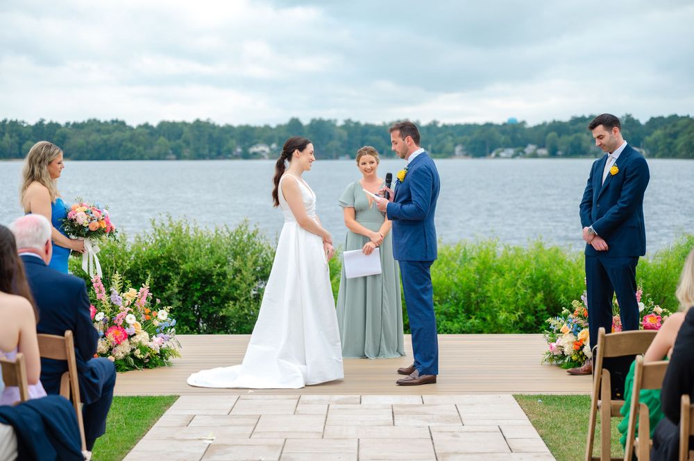 Scenic waterfront outdoor wedding ceremony with guests seated in white chairs overlooking harbor in Massachusetts