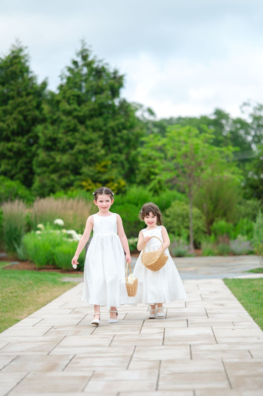 Two flower girls in white dresses walk down a stone aisle during a wedding at the Lakehouse in Halifax, MA.