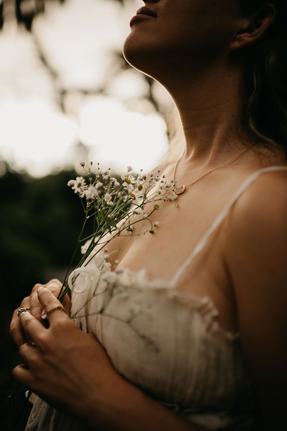 Artistic close-up series of delicate white flowers held against a soft white dress in moody lighting. sarasota maternity photographer
