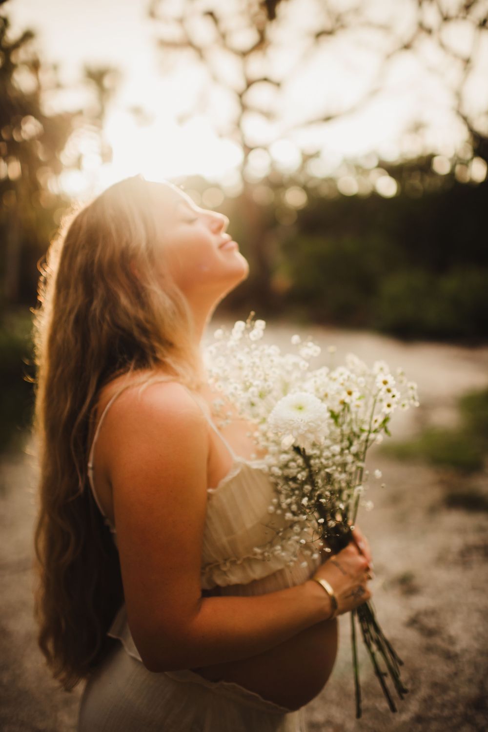 A person holds a bouquet of baby's breath flowers while basking in golden sunlight during a dreamy outdoor photoshoot. Sarasota best family