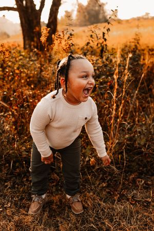 An excited young child with braids laughs loudly while playing in a golden autumn field outdoors.