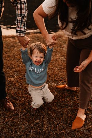 Toddler named William being swung by parents hands laughing outdoors in autumn setting.