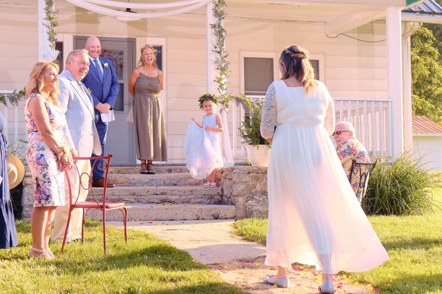 A wedding ceremony takes place in a backyard with pink draping and decorative floral arrangements.