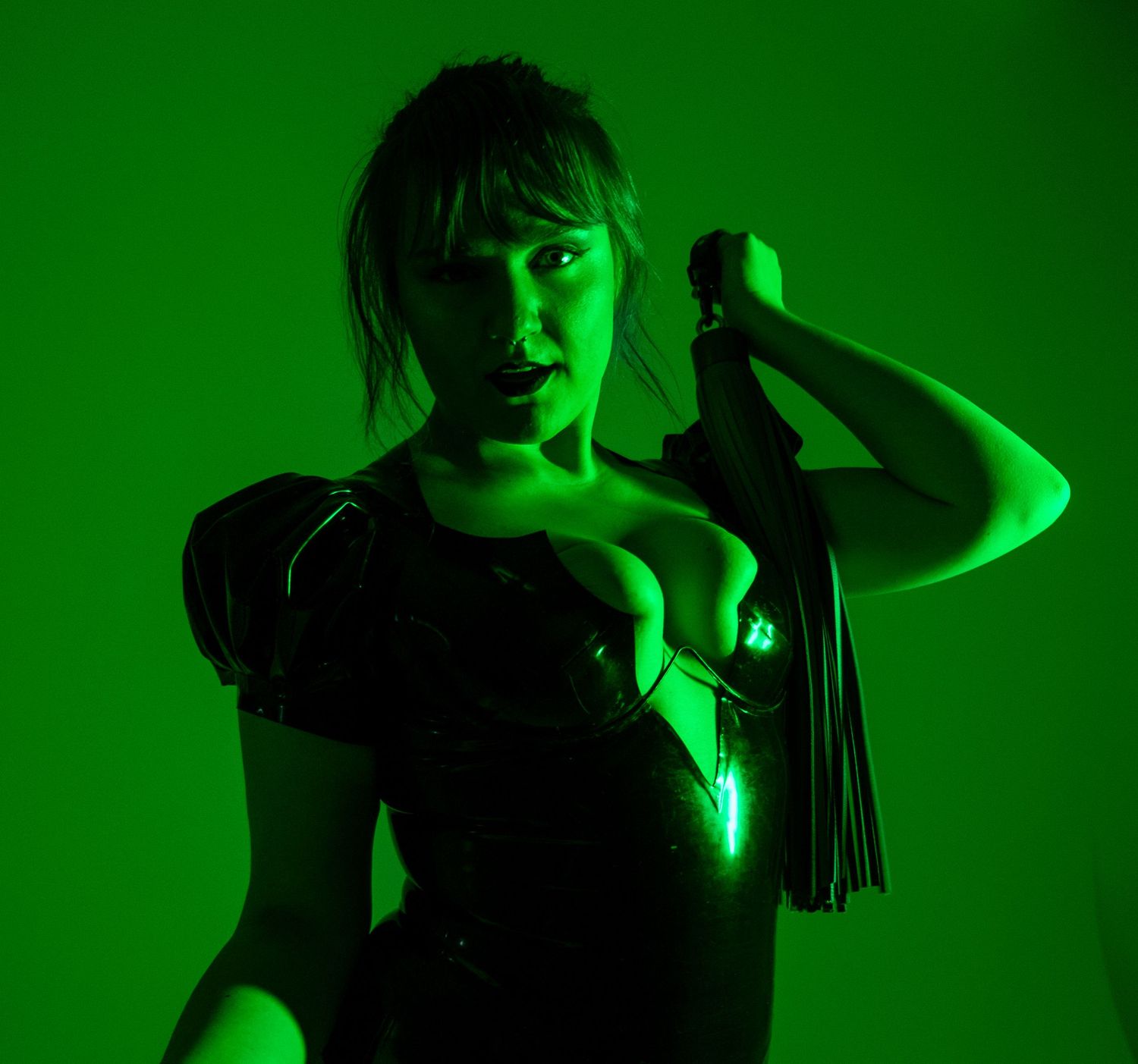 A person stands in dramatic green lighting while holding a microphone, creating a moody atmospheric portrait.
