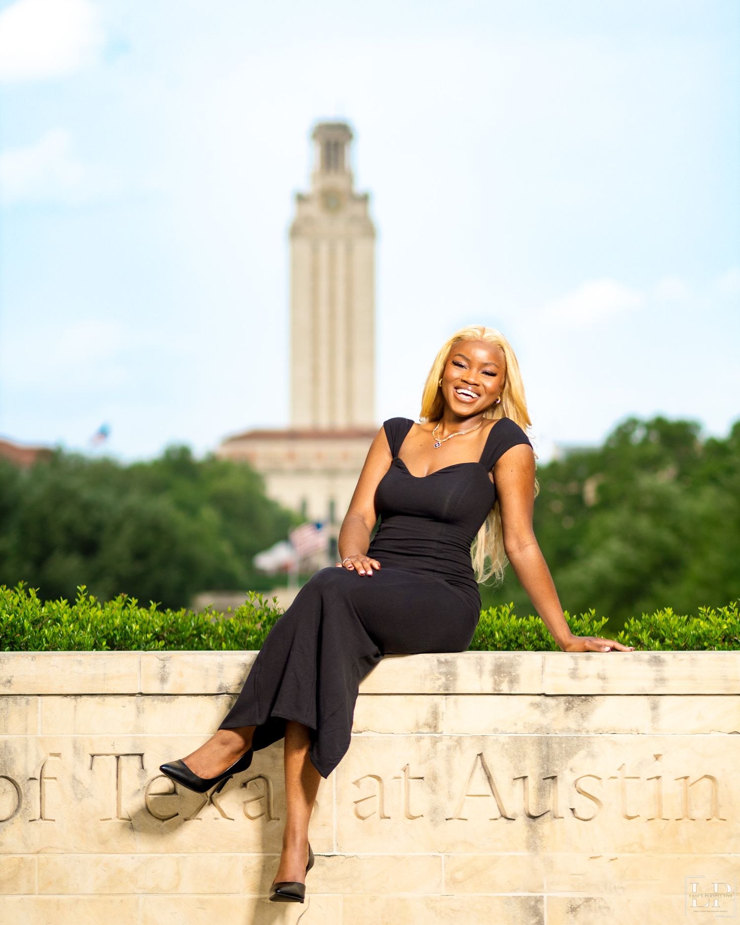Black dress photoshoot against stone wall with UT Austin tower in background.