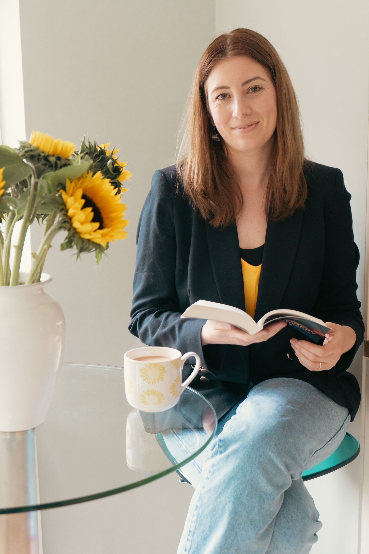 Person in business attire sitting with sunflowers and coffee mug on glass table.