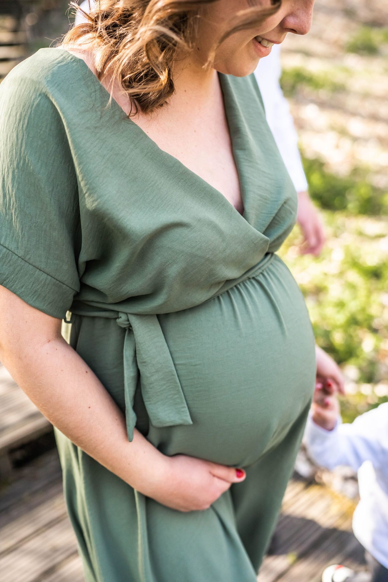 Close-up of a pregnant woman in a sage green wrap dress showing her baby bump.