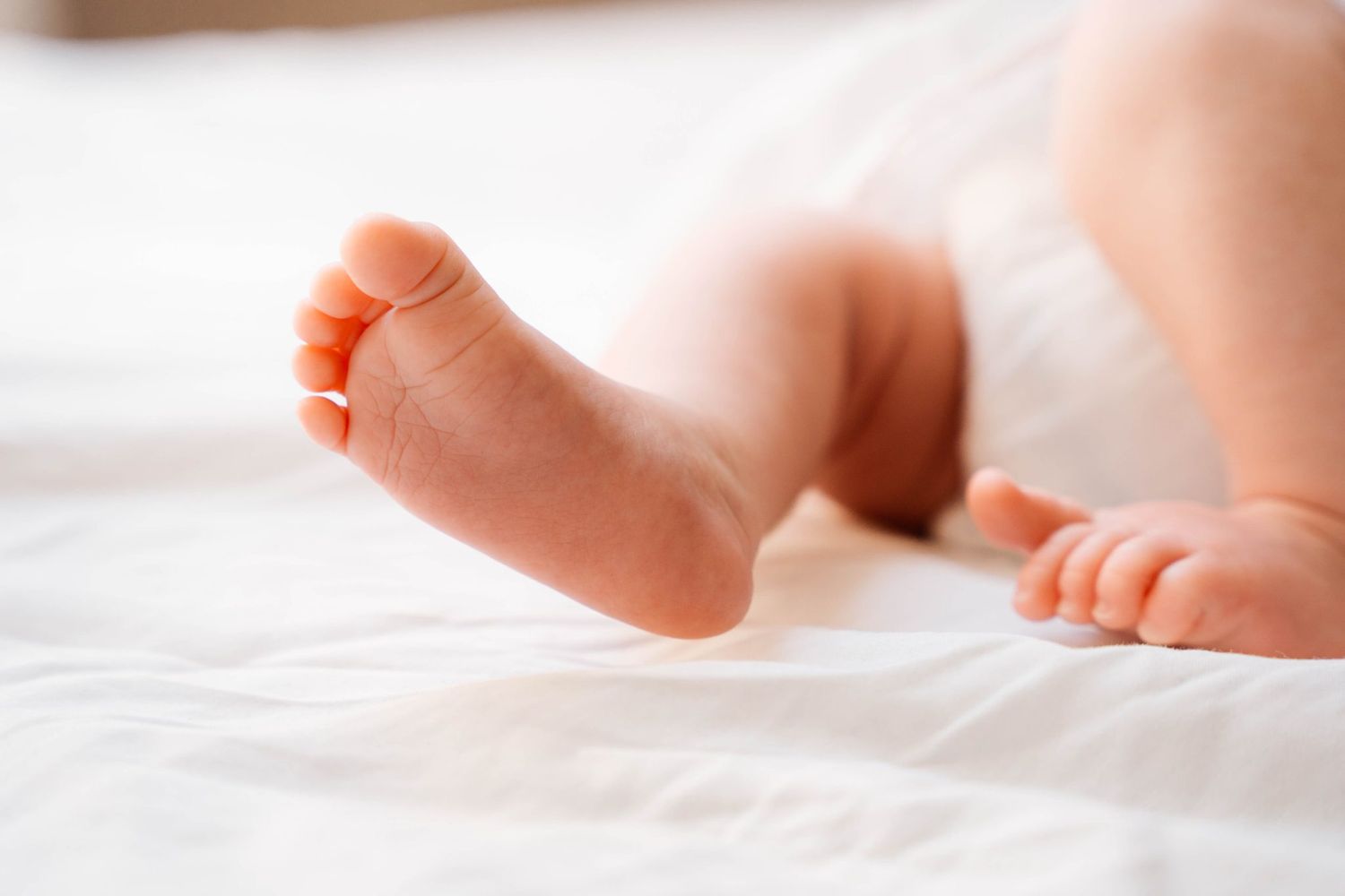 Close-up of tiny baby feet resting on white bedding.