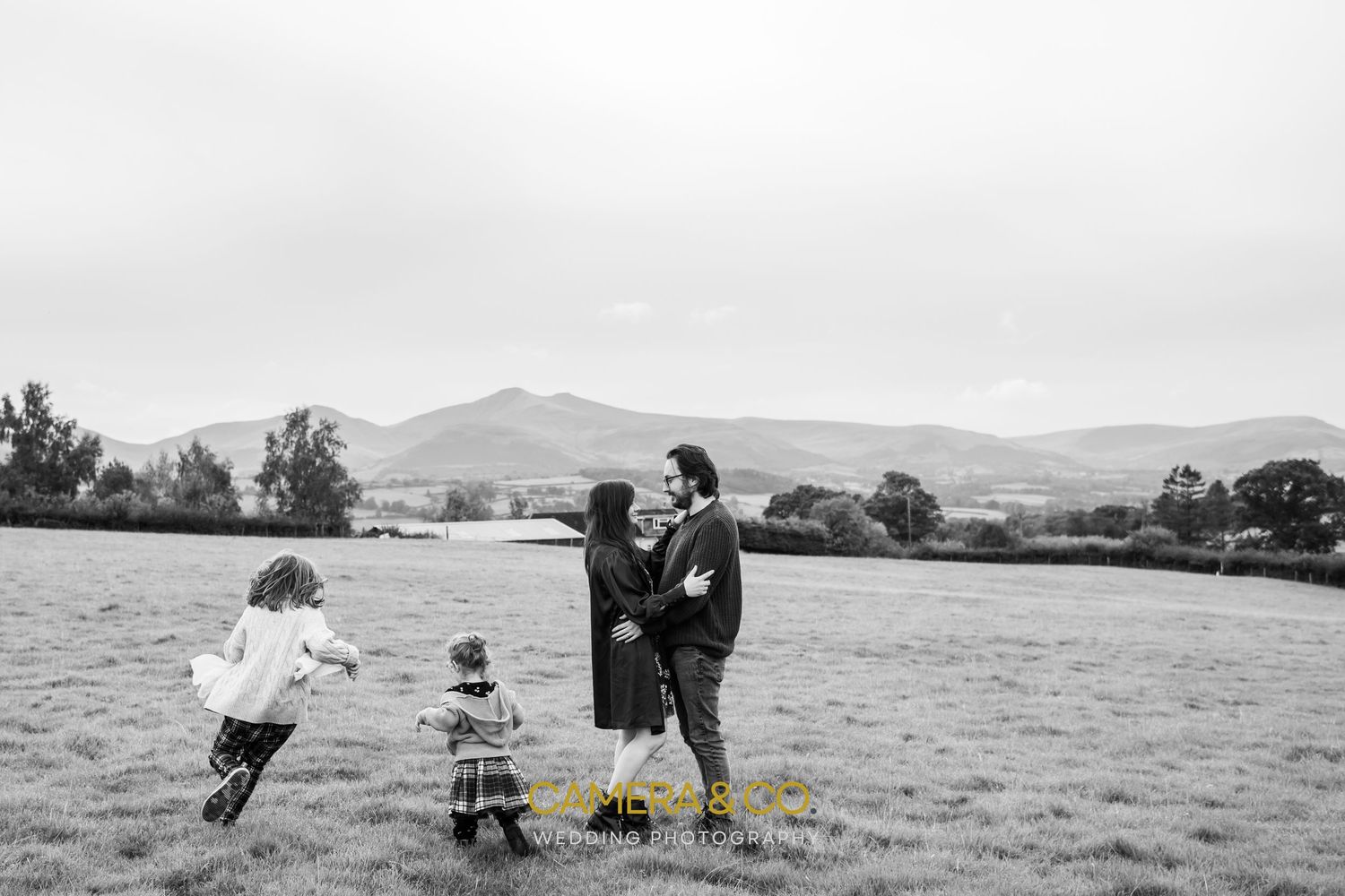 A heartwarming moment captured in black and white on a grassy field with rolling hills in the background.