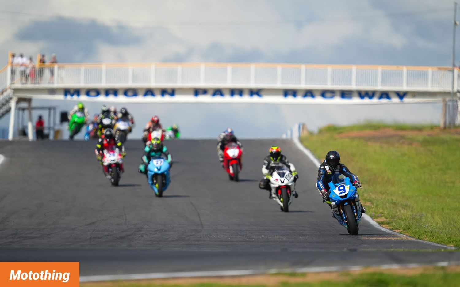 Multiple motorcycles racing along Morgan Park Raceway track under cloudy skies.