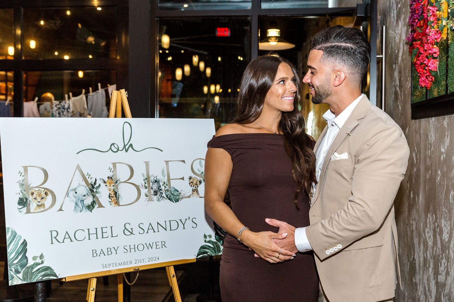 Couple posing by elegant baby shower sign with floral decor.