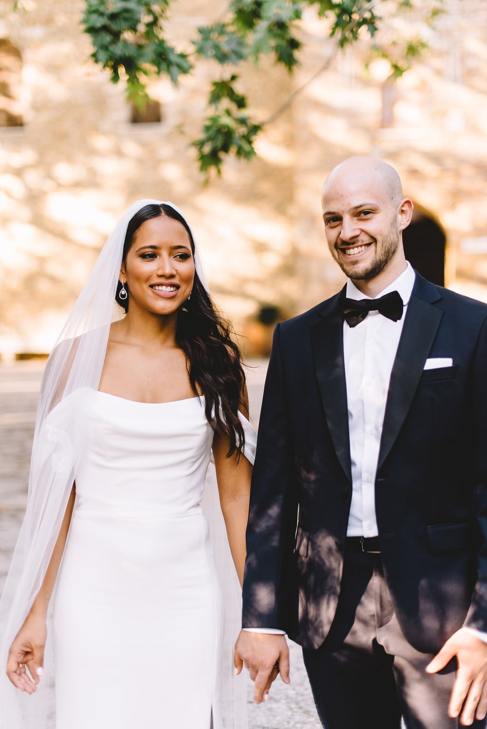 Bride in white gown with veil and groom in black tuxedo smiling together on their wedding day.