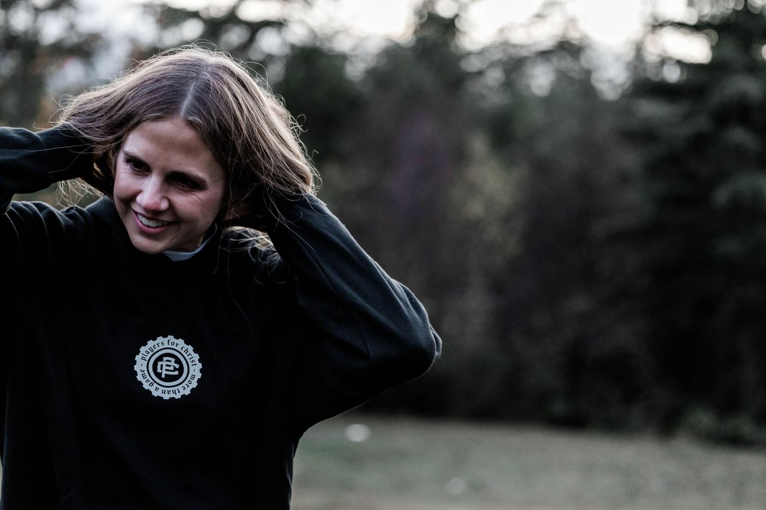 Person in black sweatshirt with circular logo poses outdoors against natural background.