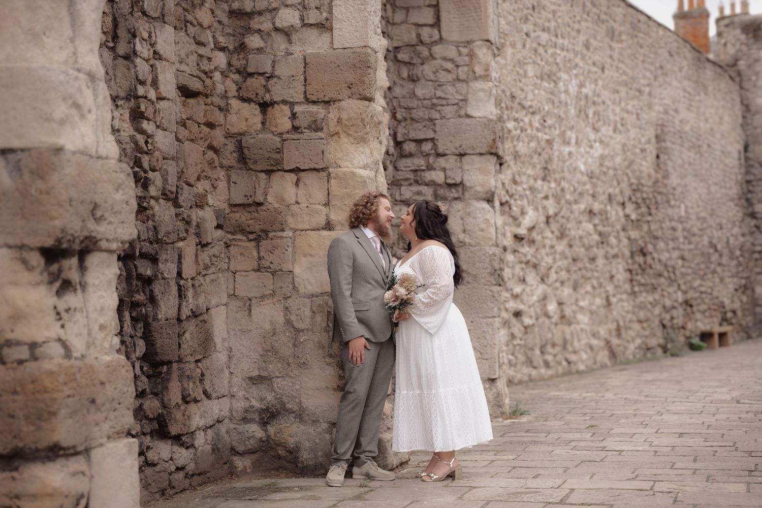 Newlyweds share intimate moments against a rustic stone wall background.