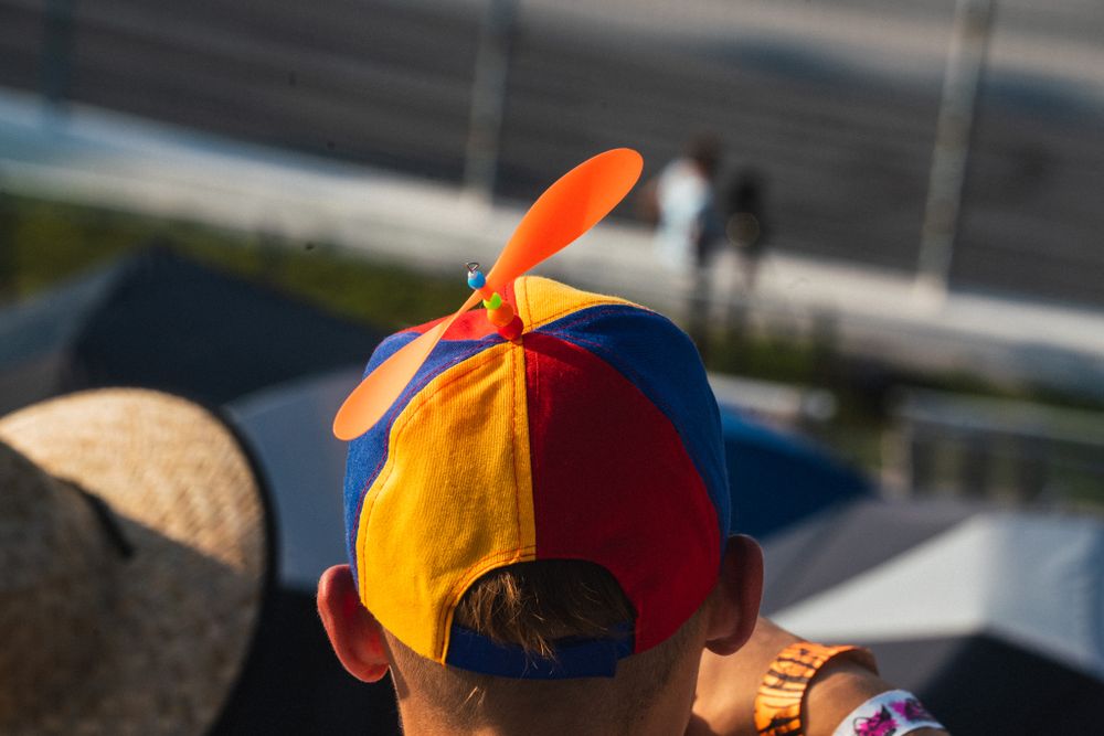 A colorful propeller hat with an orange spinning blade is worn by someone at an outdoor event.