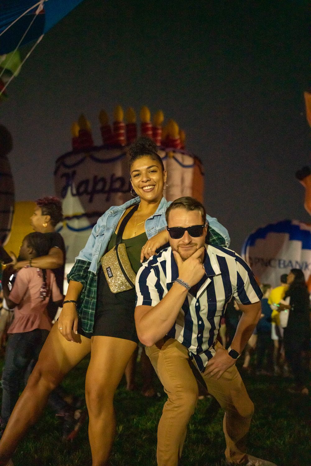 People having fun at a nighttime festival with a large birthday cake decoration in the background.