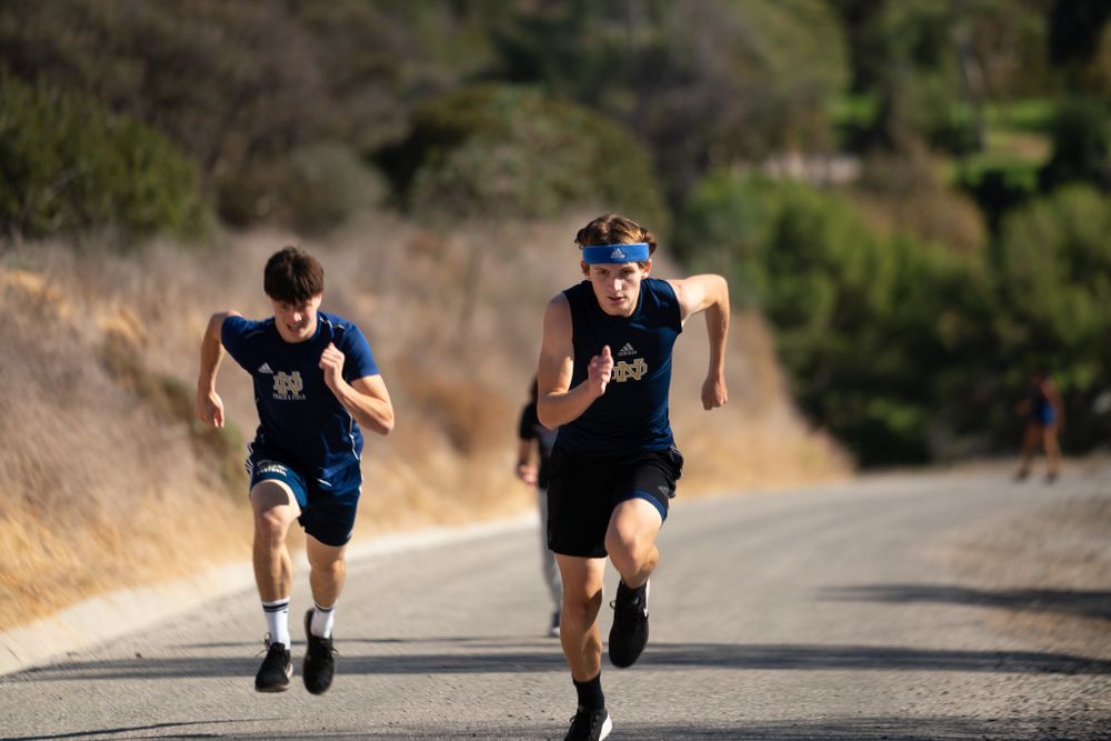 Two runners sprinting uphill on a dirt trail during outdoor workout.