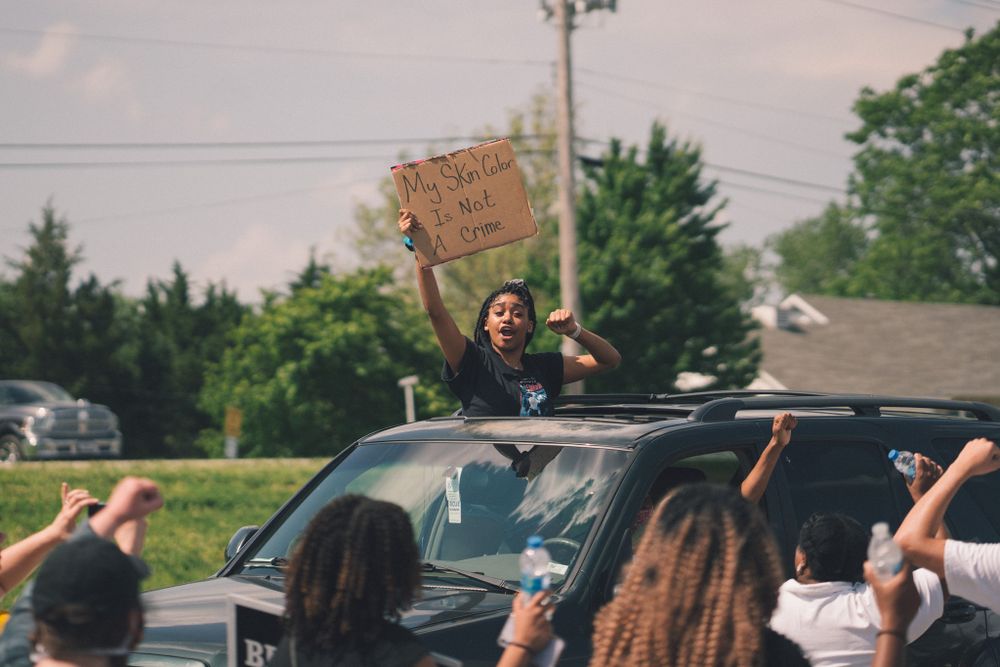 Protesters gathering around cars with raised signs during a demonstration.