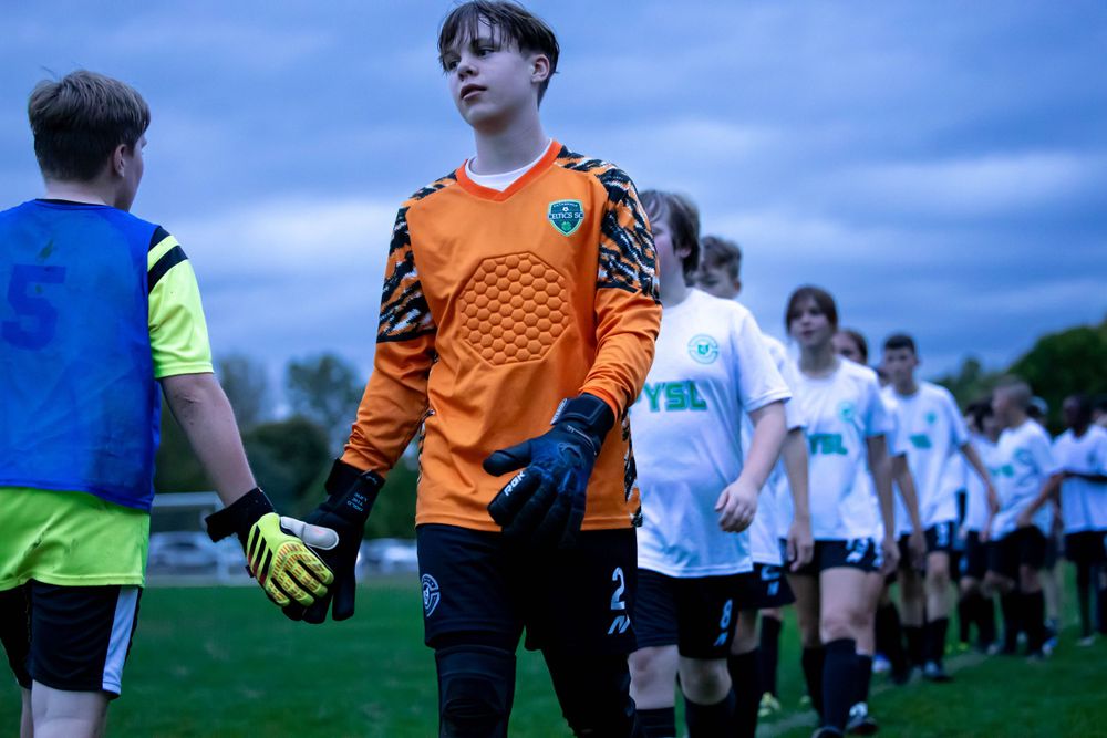 Soccer goalkeeper in orange jersey prepares for team lineup before match.
