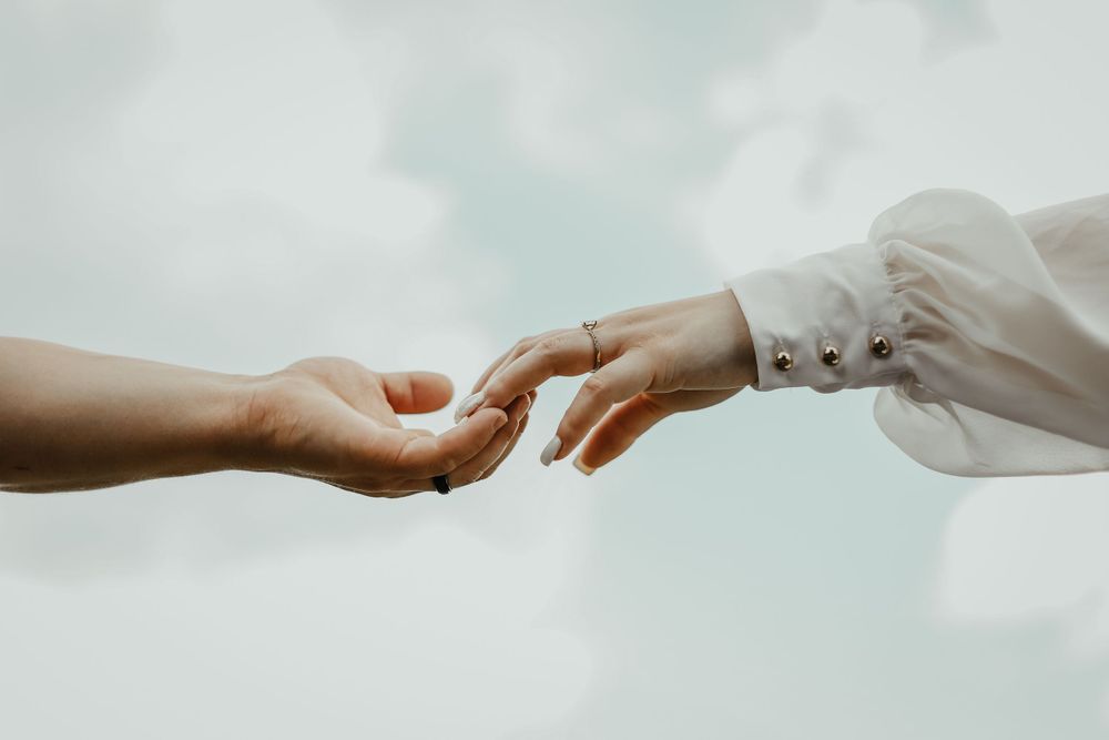 Two hands reaching towards each other against cloudy sky in romantic gesture.
