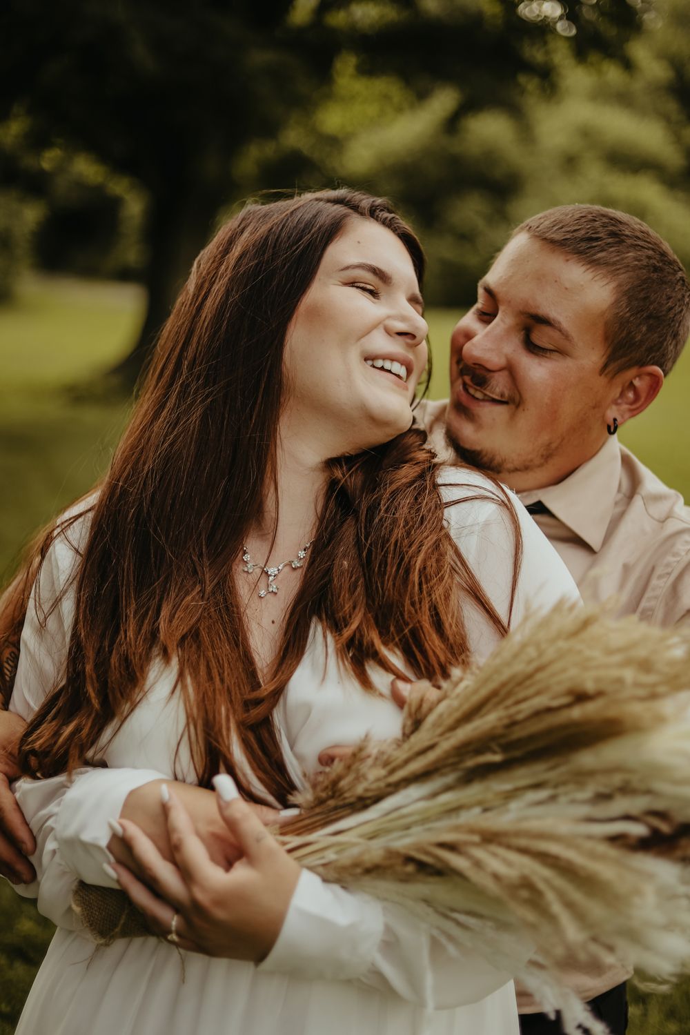 Joyful couple laughing together outdoors while holding dried wheat stems.