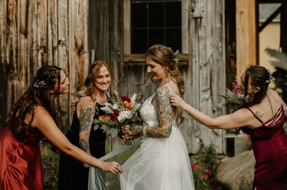 A joyful moment between a bride and her bridesmaids outside a rustic barn.