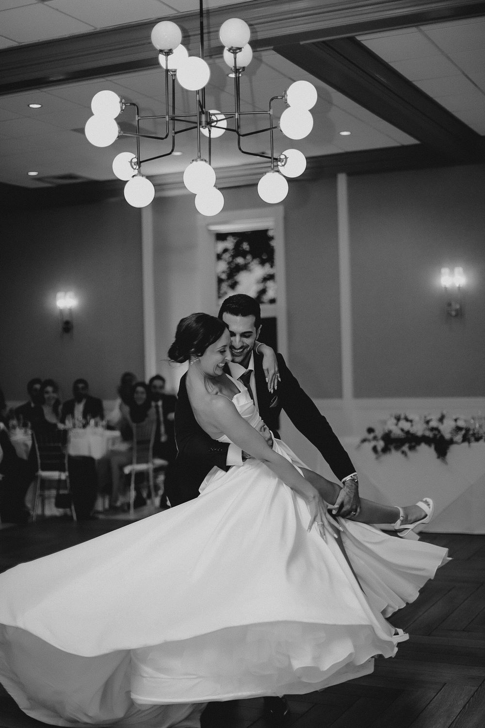 A couple dancing at their wedding reception under a modern globe chandelier.