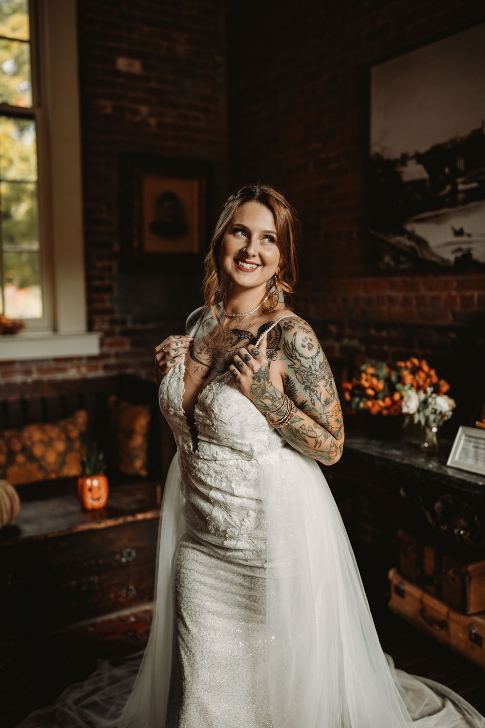 Stunning bride in lace sleeve wedding dress with tattoos poses in rustic brick interior.