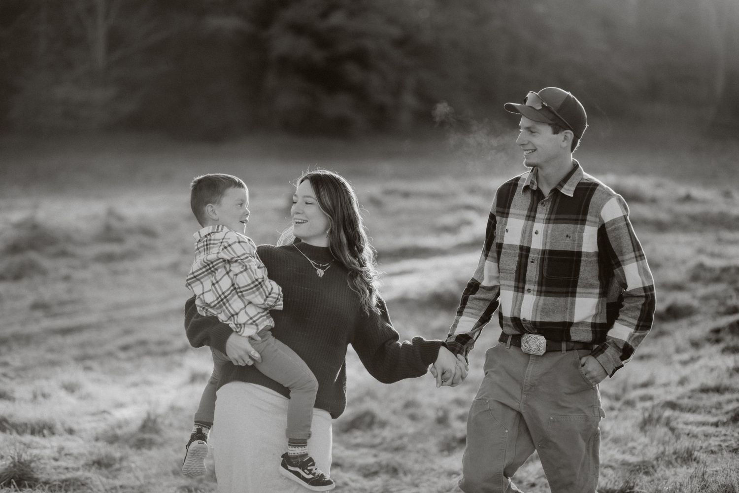 A black and white family portrait captured in a misty field at sunset.