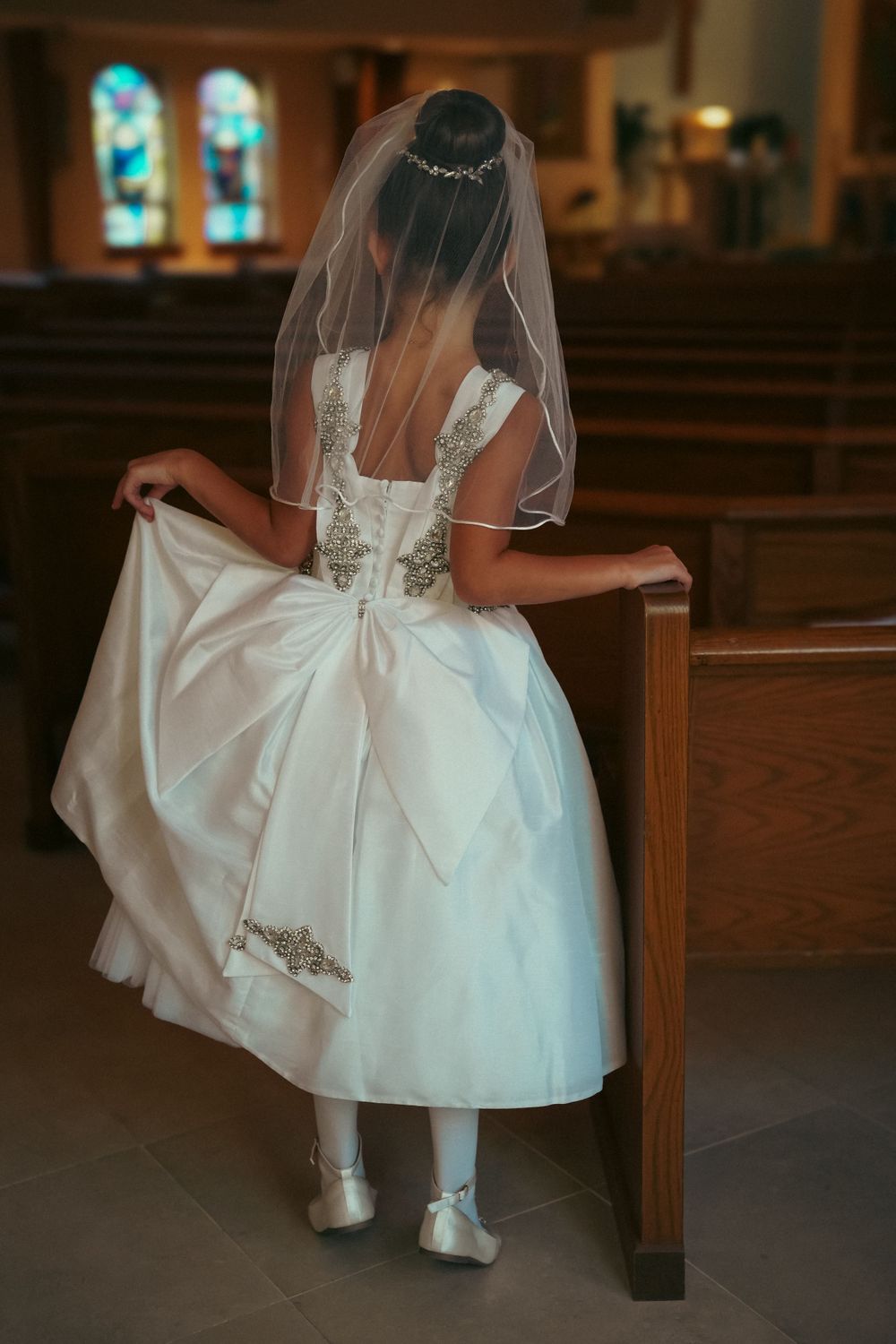 White wedding dress with lace details and bow shown from behind in church pews.