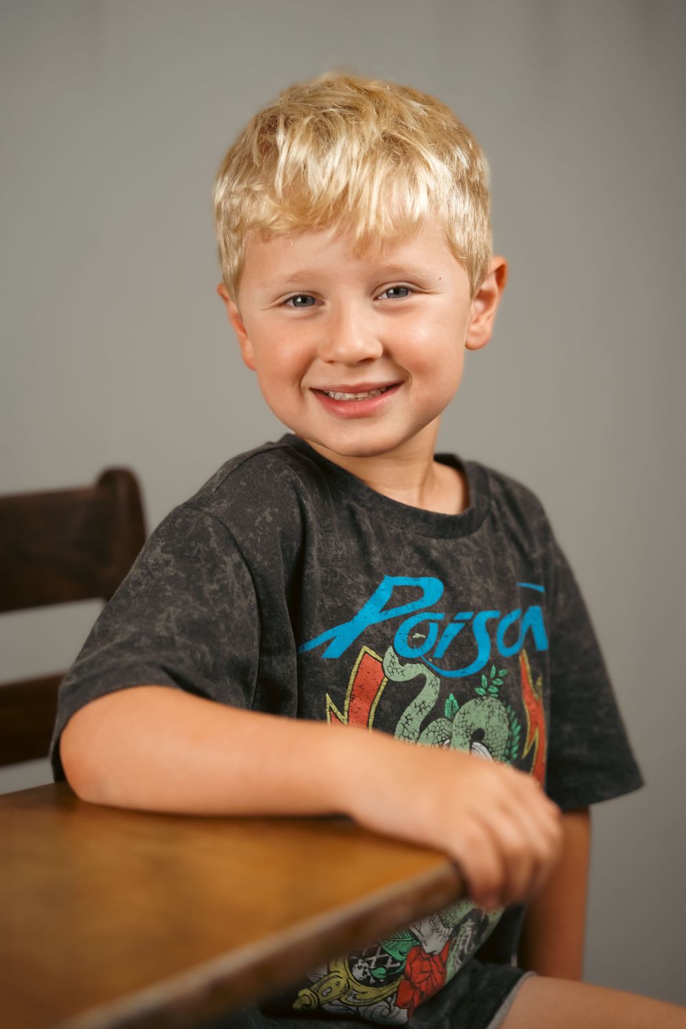 Child wearing a dark t-shirt with graphic design sitting at wooden table.