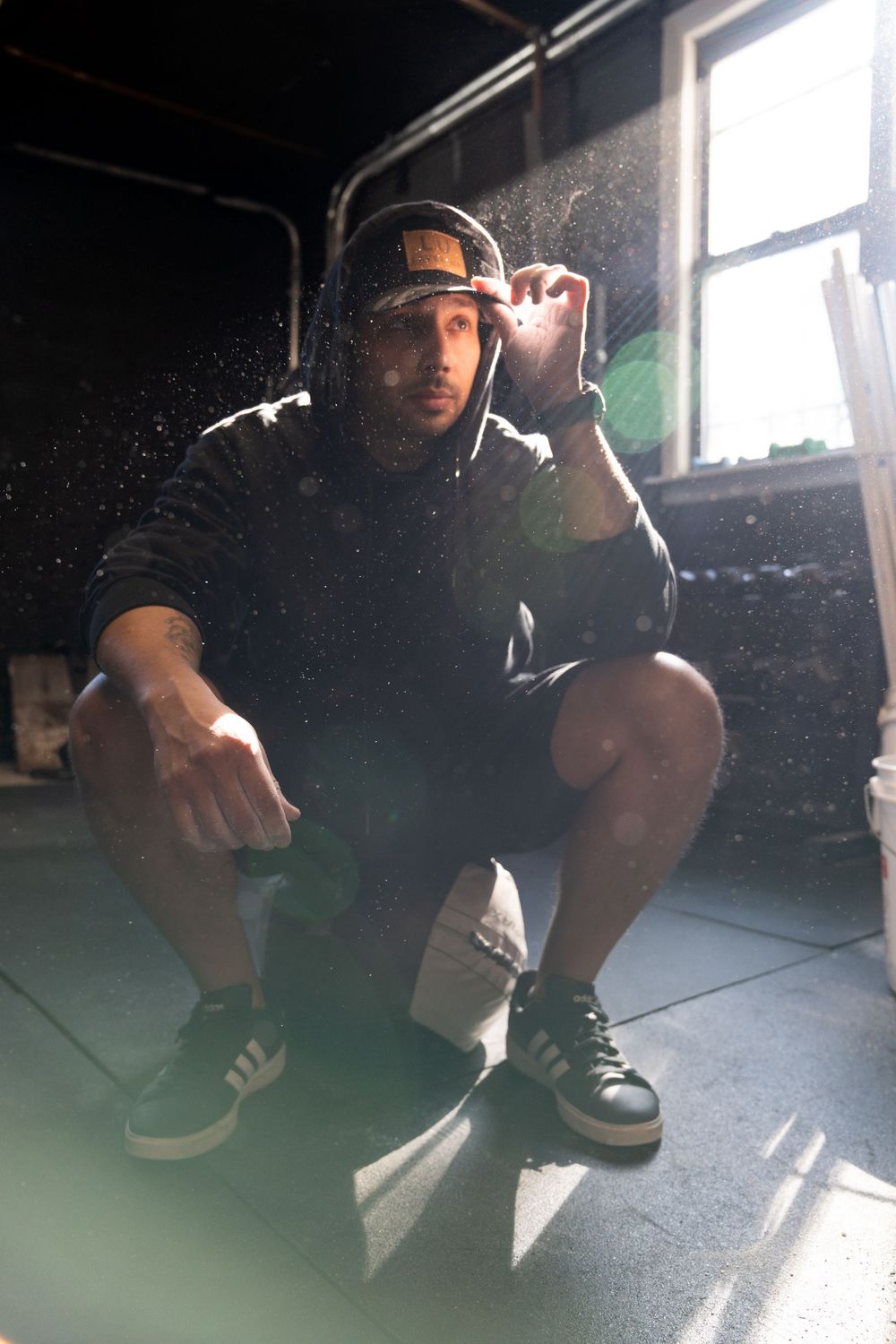Person in dark clothing crouching in dramatic sunlit room with shadows.