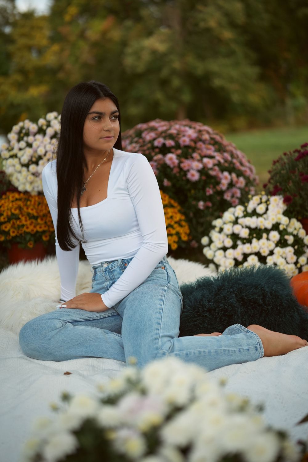 Person in white top and jeans reclining among colorful autumn garden flowers.