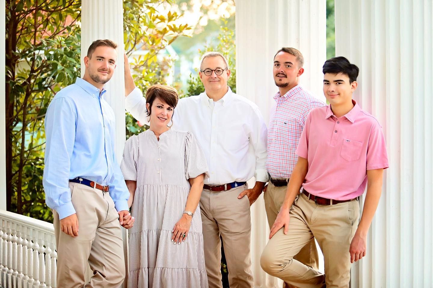 Family group poses together in front of white columns wearing coordinated casual attire.