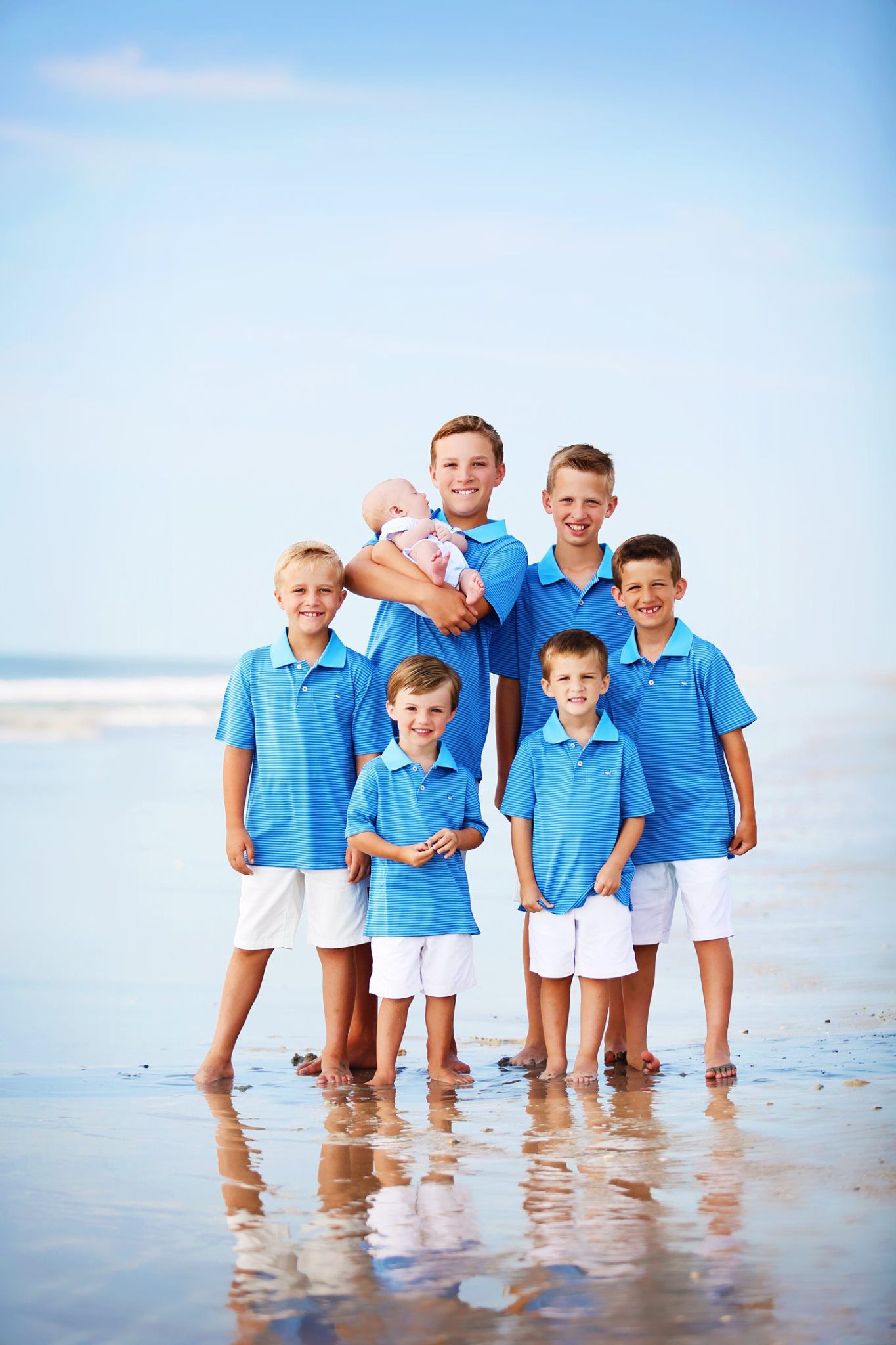 Group of boys in matching light blue polo shirts and white shorts posing together on a beach.
