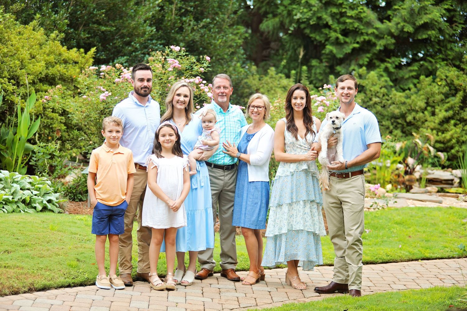 Multi-generational family poses together in a lush garden setting on a summer day.