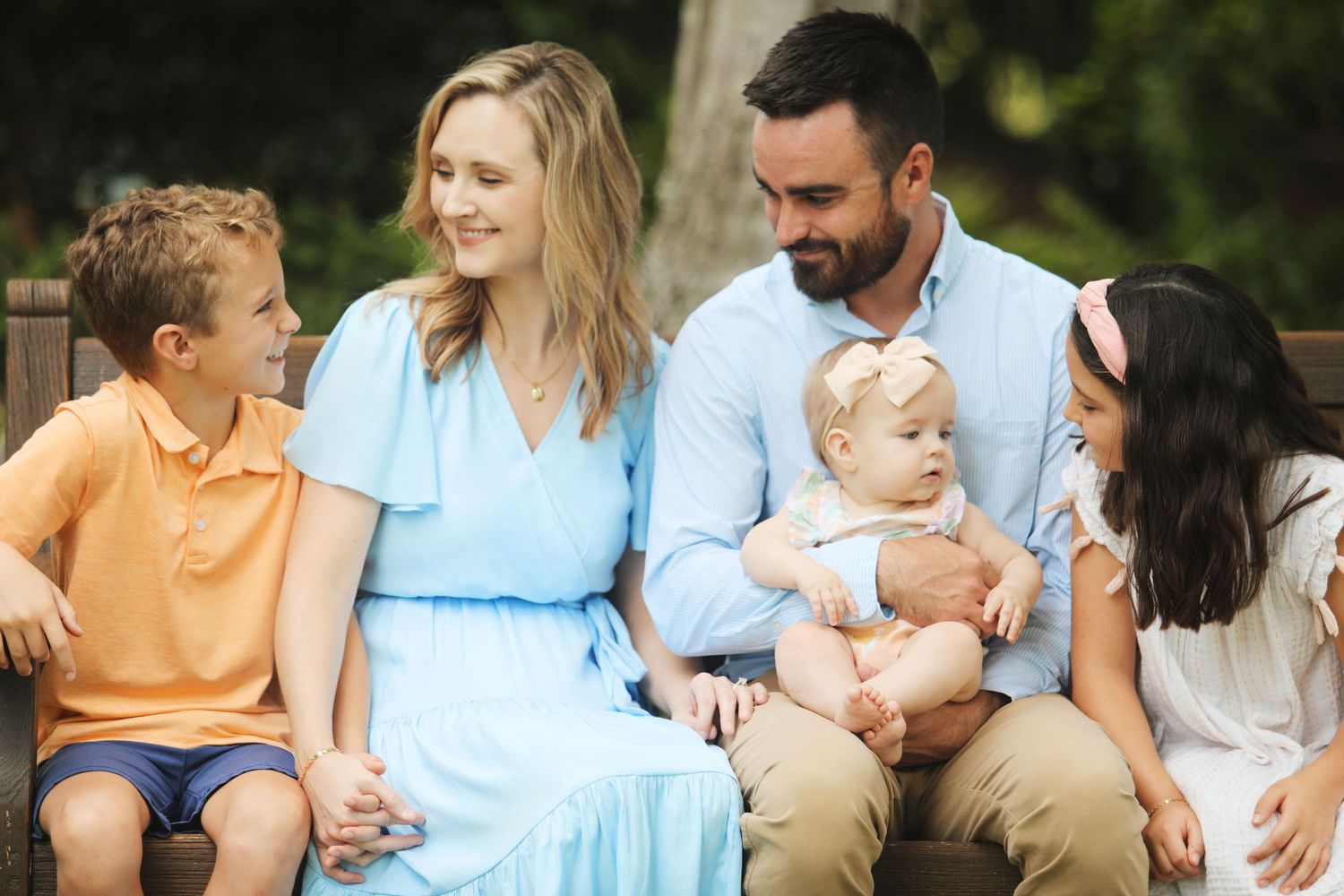 Happy family sitting together outdoors on sunny day wearing casual summer clothes.