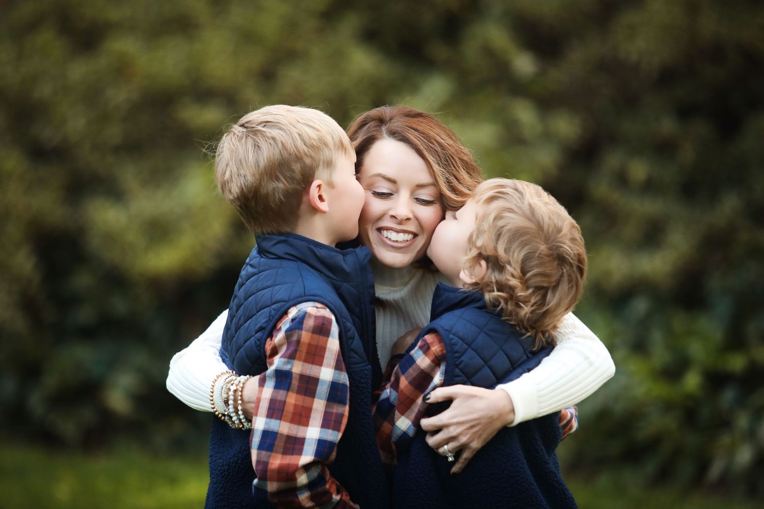 A warm embrace between two young children and a woman outdoors in a natural setting.
