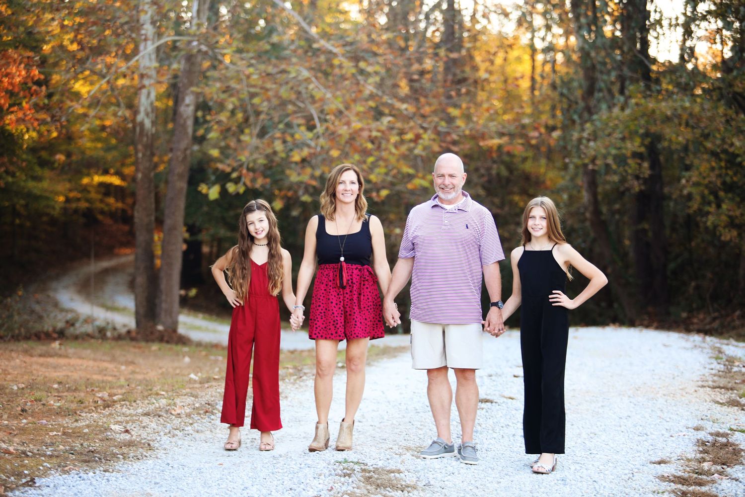 Four people in coordinated outfits pose on a gravel path during autumn.