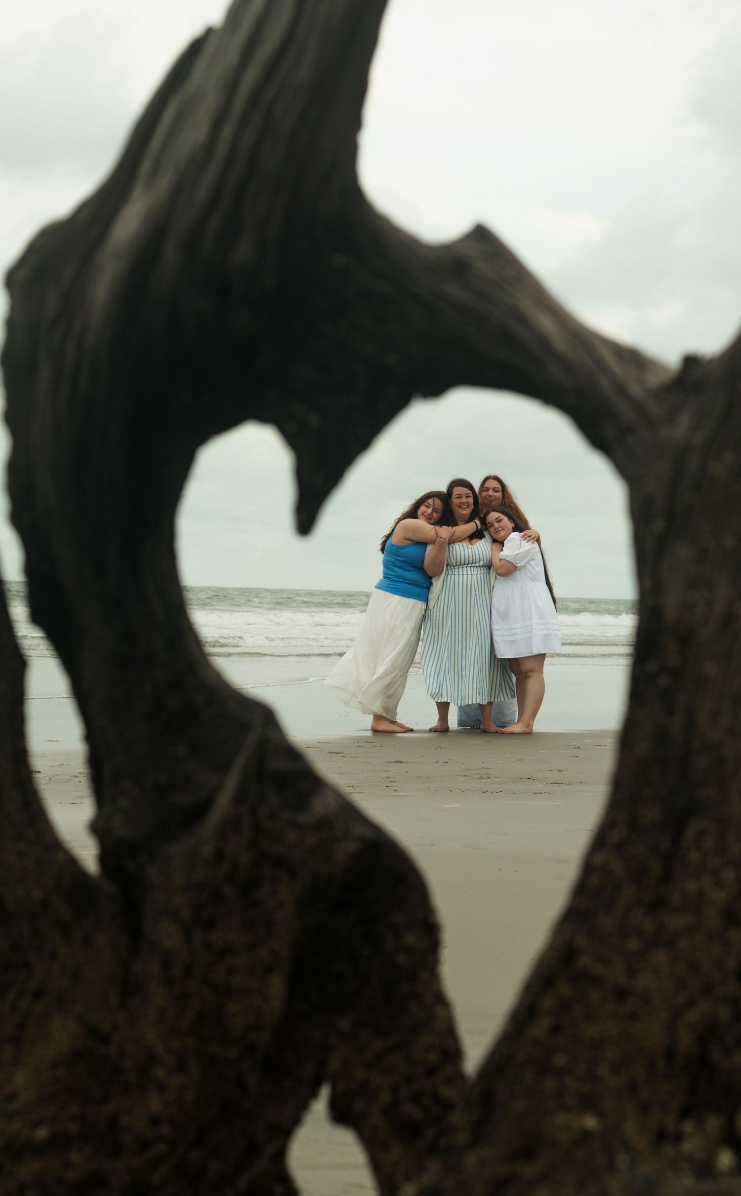 Group of friends standing together at beach during sunset with ocean waves in background.