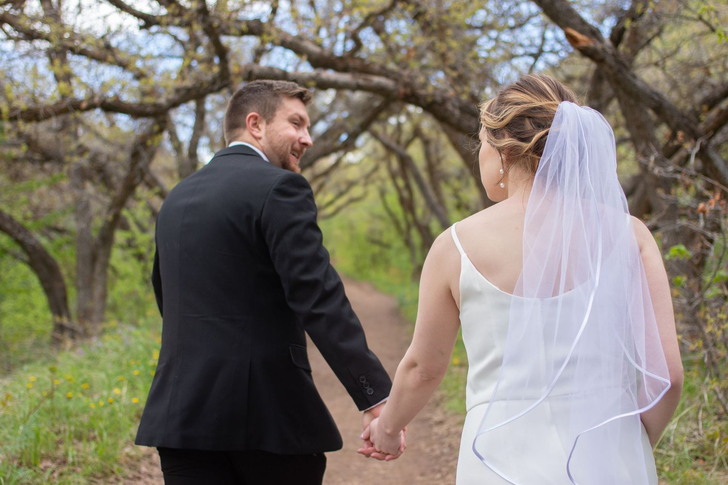 Bride and groom walk away from camera hand in hand at their garden venue in Salt Lake City, Utah.