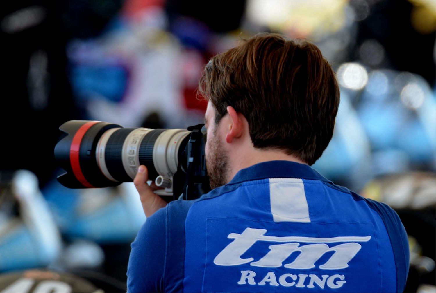 Photographe de course avec téléobjectif portant le maillot de l'équipe TM Racing capturant l'action sur la piste.