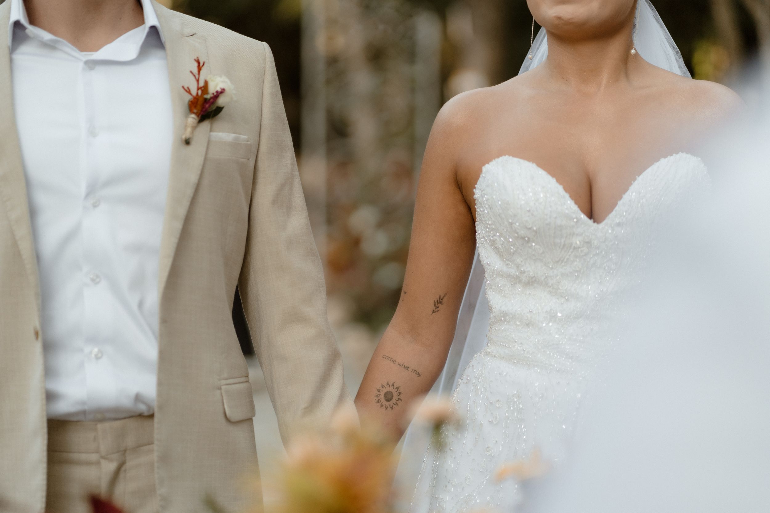 Wedding party members stand together in white dresses and tan suits outdoors.
