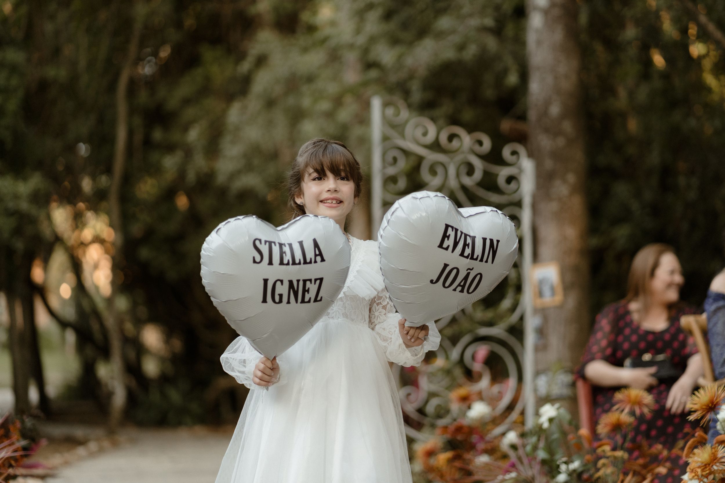 A person in a wedding dress holds two white heart-shaped signs with names written on them.