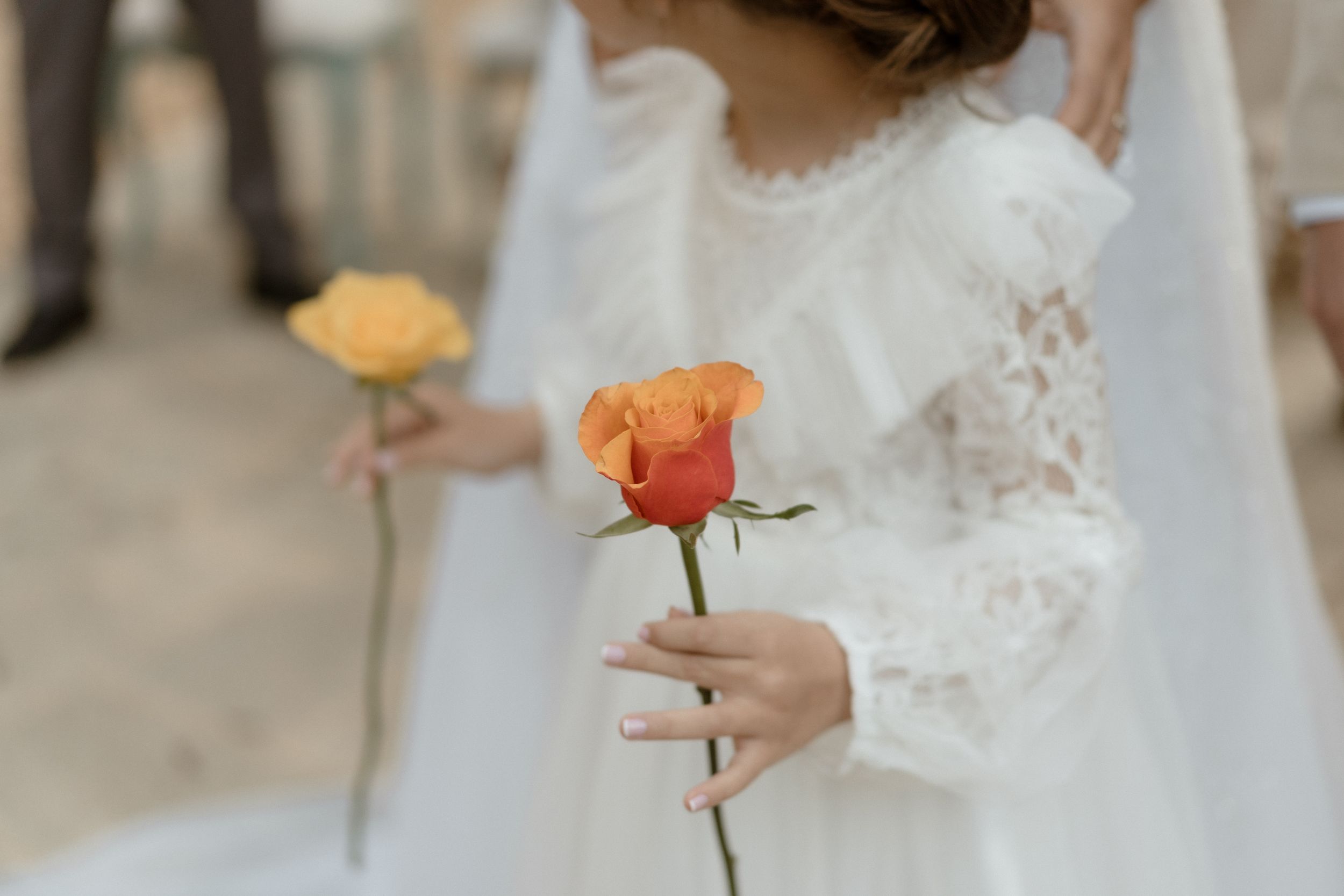 Close-up shot of a single orange rose being held against a white wedding dress.