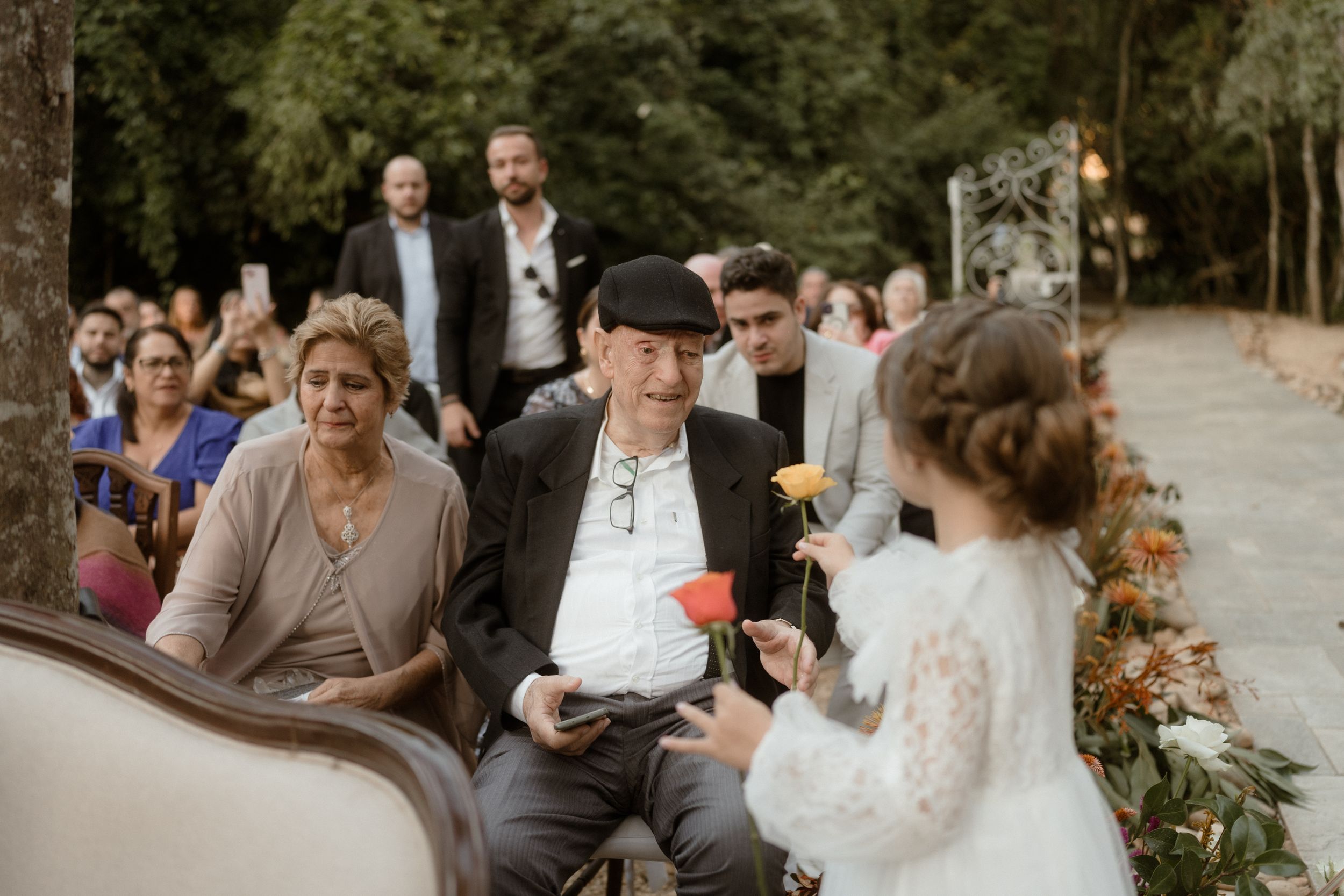 Wedding guests seated outdoors watching the ceremony proceedings with decorated aisle behind them.