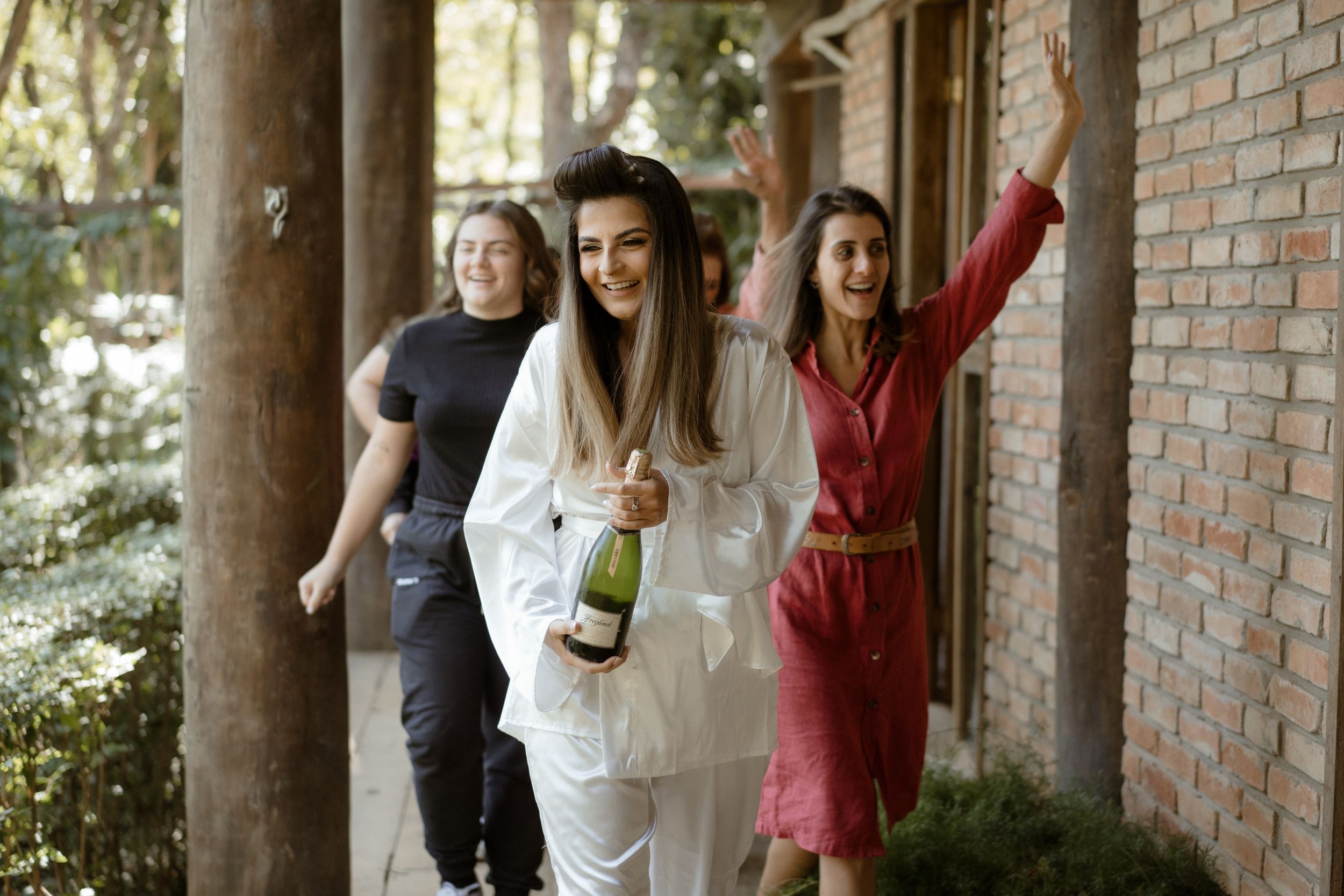 A joyful celebration outdoors with champagne and laughter near a brick colonnade.