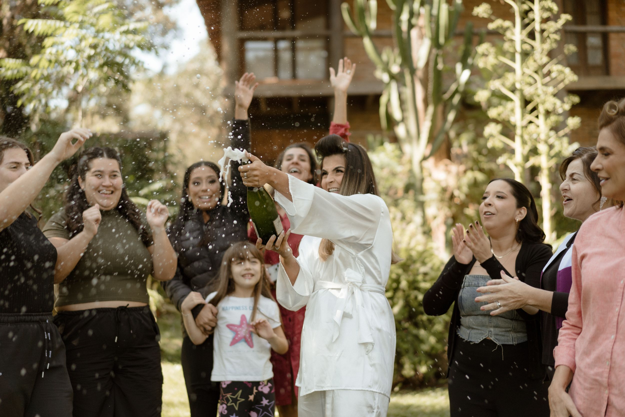Friends celebrate with champagne spraying in the air at an outdoor garden party.
